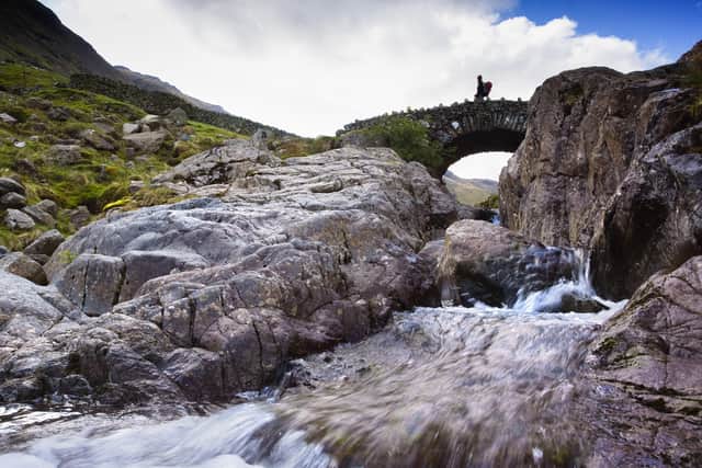 A hiker crosses Stockley Bridge from Seathwaite Fell in the Lake District, Cumbria UK.