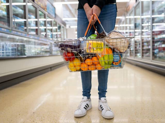 A woman holds a basket of goods in a supermarket.
