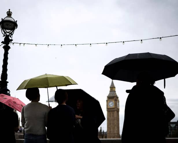 Pedestrian stand under umbrellas while looking at Elizabeth Tower, commonly called Big Ben from the Southbank by the River Thames, in central London, on July 31, 2023 on a gloomy and rainy summer day.