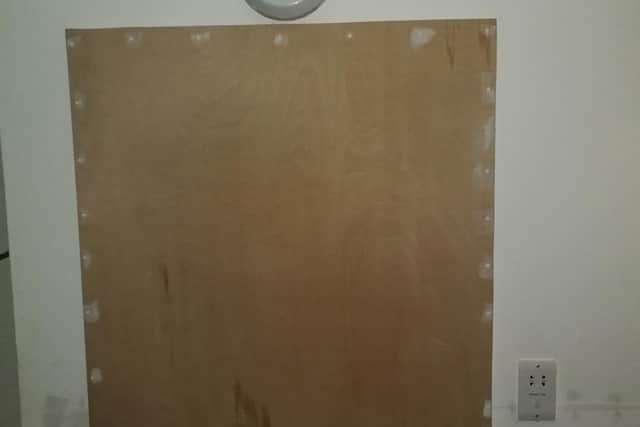 Board covering damp and mould on bathroom wall from major leak in adjacent flat