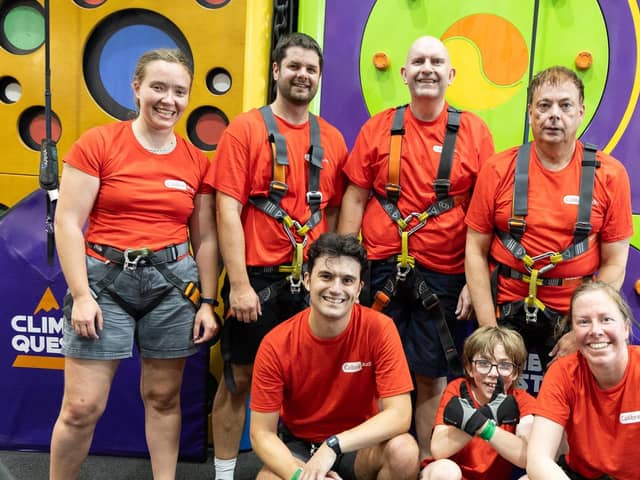 Image shows the seven members of the Calibre Climb Team standing in front of a climbing wall wearing red Calibre Audio T-shirts and climbing harnesses. Photo from Andy Scott Photohello