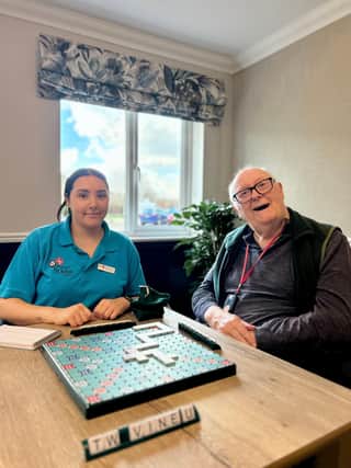 Rebecca Major, Activities Co-ordinator, with Meadowcroft resident Michael laughing together and playing Scrabble.