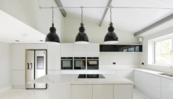 The kitchen features sleek white cabinetry with quartz countertops throughout, integrated and wifi-controlled Neff ovens, Miele integrated wine cooler, an integrated Bosch fridge-freezer, dishwasher, and washing machine, an additional Samsung American style fridge-freezer with 21.5 inch HD multimedia touch screen system, and a large central island.